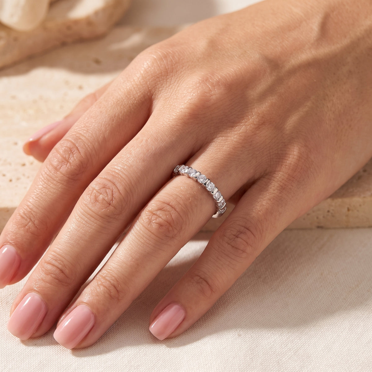 Full-hand view of a silver bar-set ring with round clear stones worn on a finger.