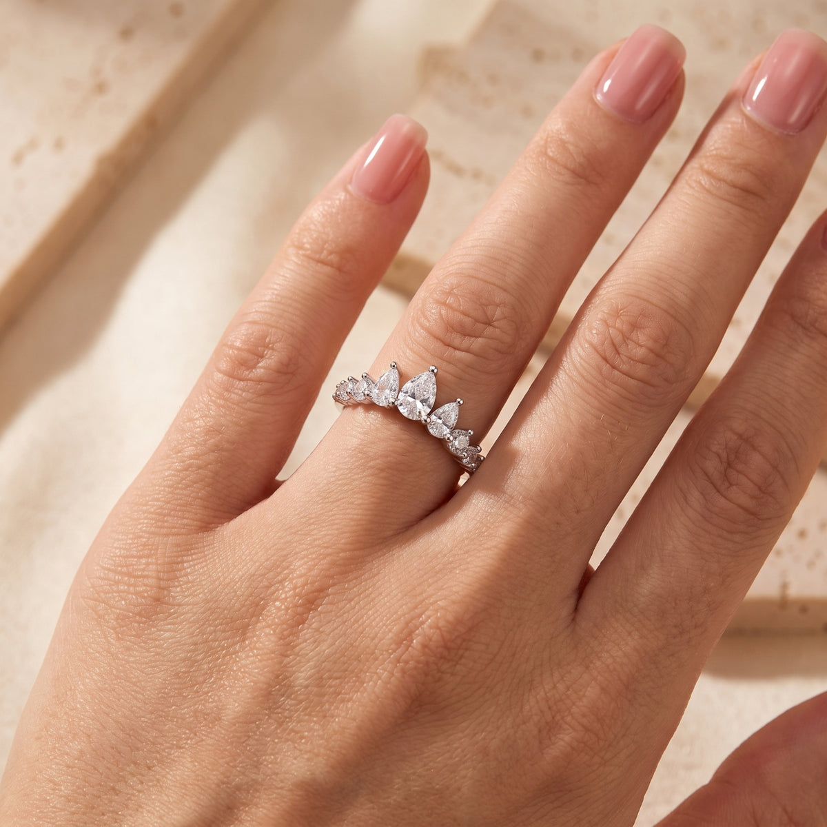 Silver pear tiara ring worn pointing upward on a model's ring finger with a soft nude manicure.