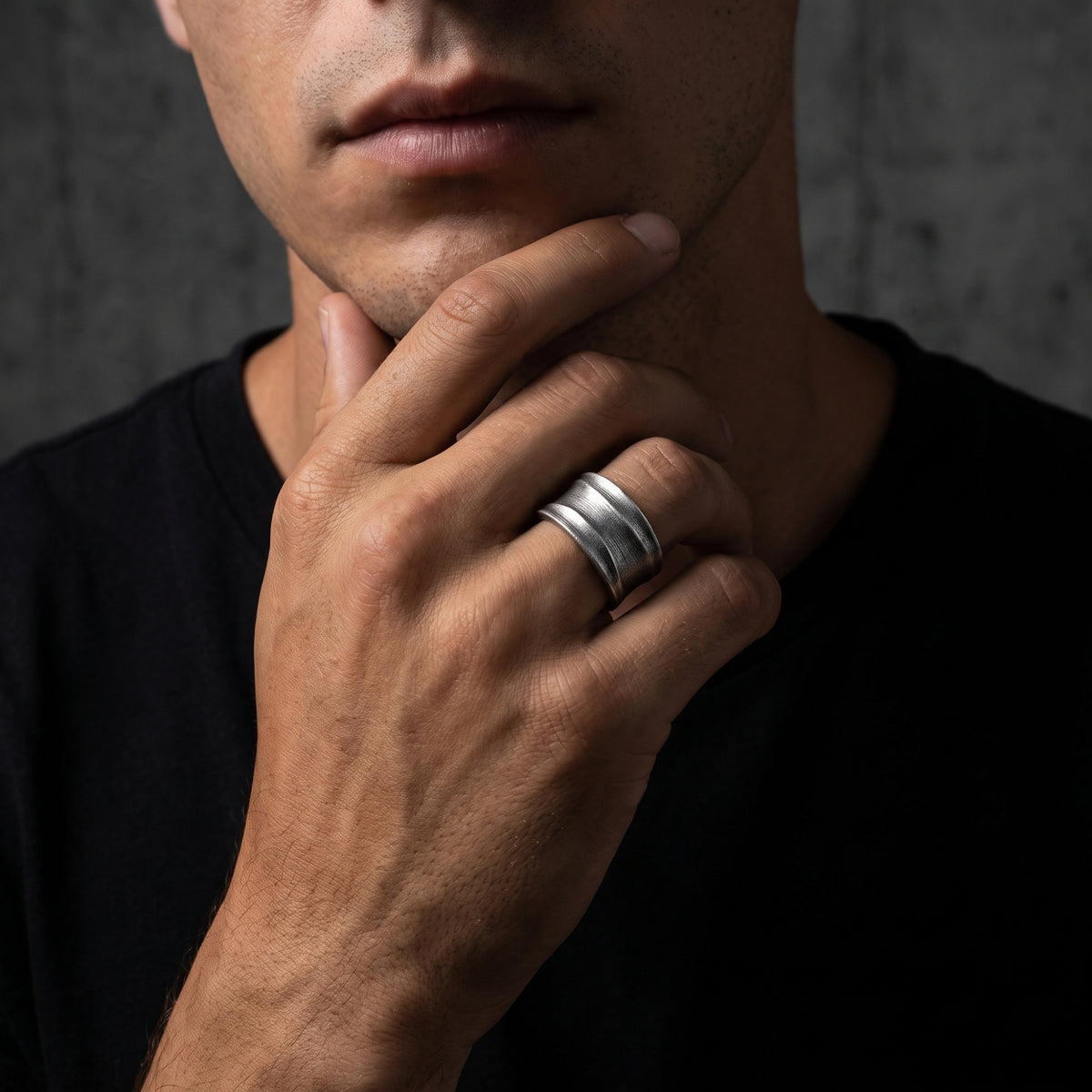 Silver ribbed open-band ring worn on a hand resting against a man's chin over a black shirt.