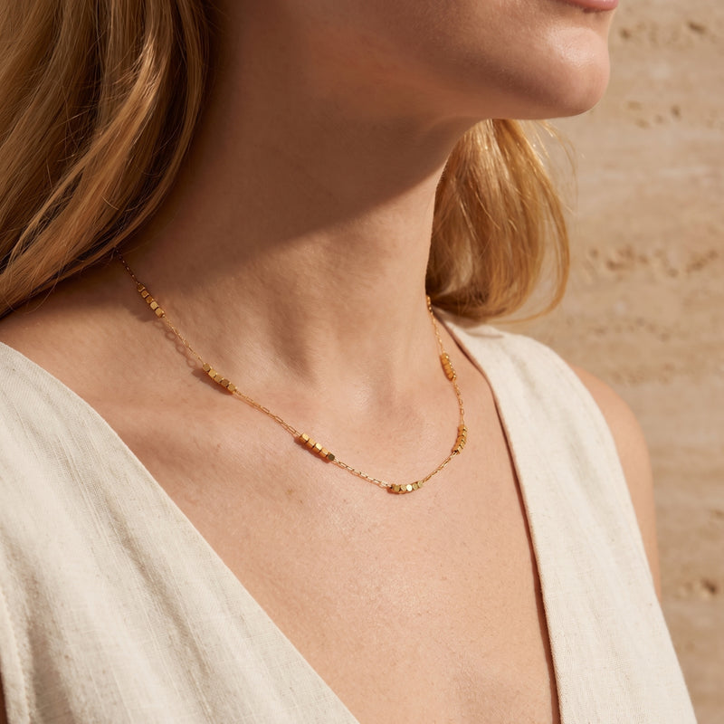 Model wearing the gold-tone cube station necklace with small metal bead clusters near her collarbone.