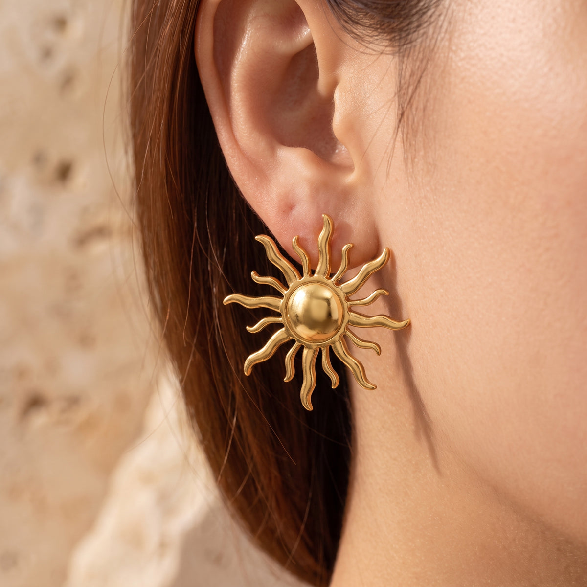 Close-up side view of a gold-tone sunburst stud earring worn on an earlobe.