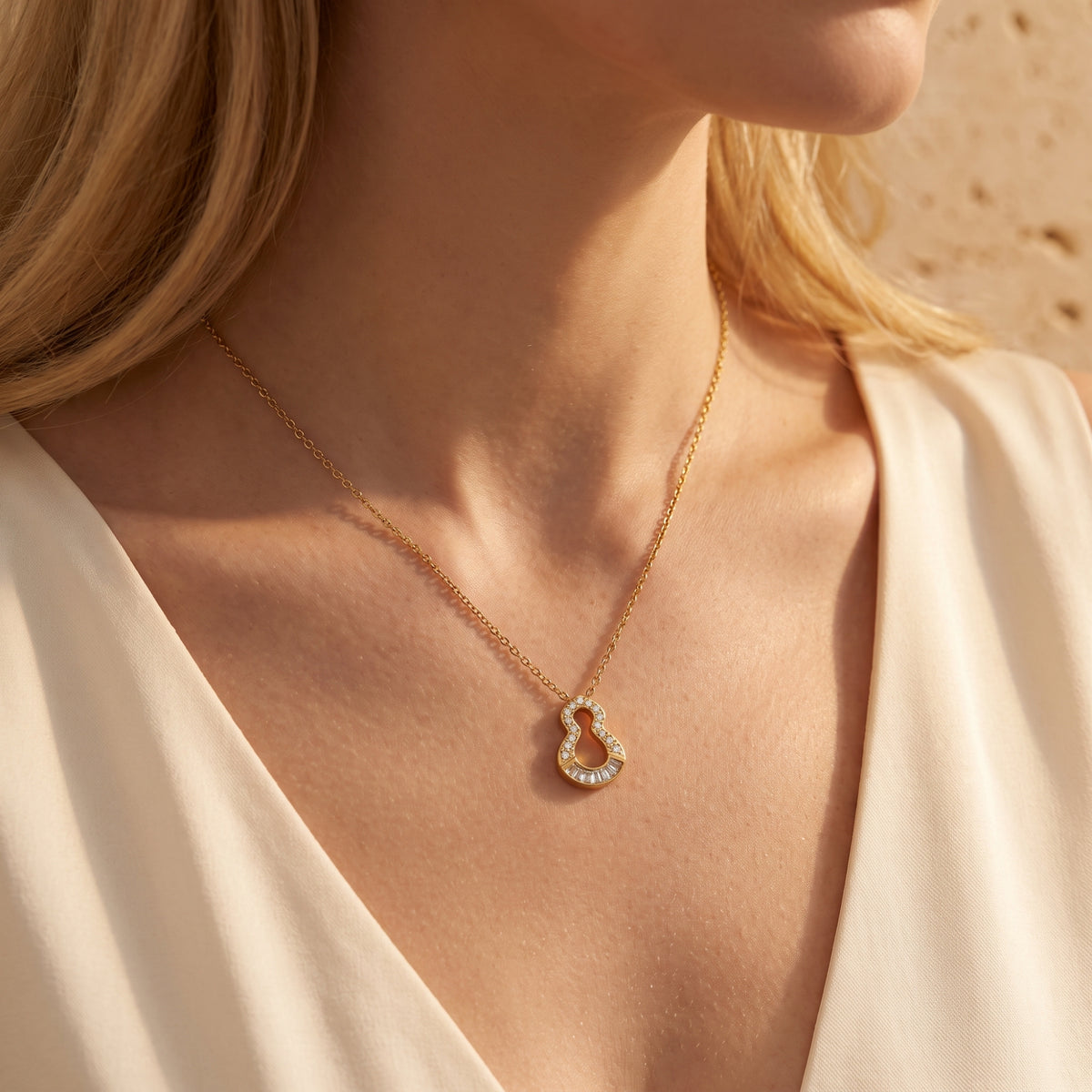 Close view of the gold-tone keyhole pendant worn on a model’s bare décolletage with a light-colored garment at the shoulders.