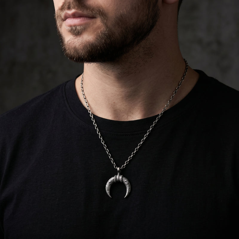 Close-up of a bearded man wearing the textured crescent pendant over a black shirt.