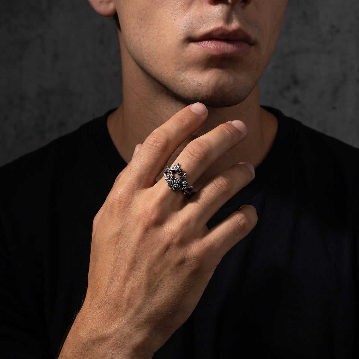 Model wearing the oxidized silver rose vine open ring on his middle finger against a dark background.