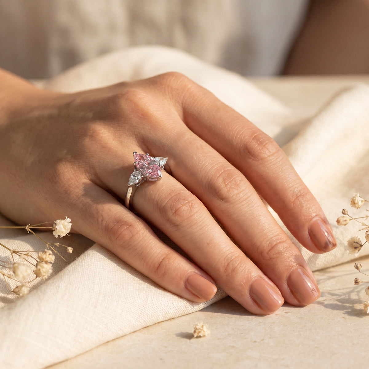 Marquise pink moissanite silver ring worn on a woman's hand against a soft fabric background.