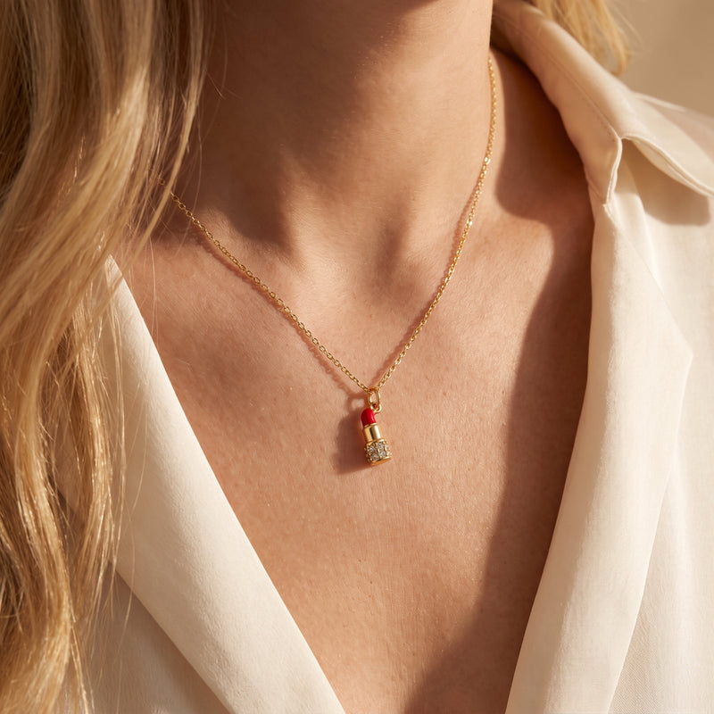 Model wearing the gold-tone lipstick pendant necklace against an open white blouse.