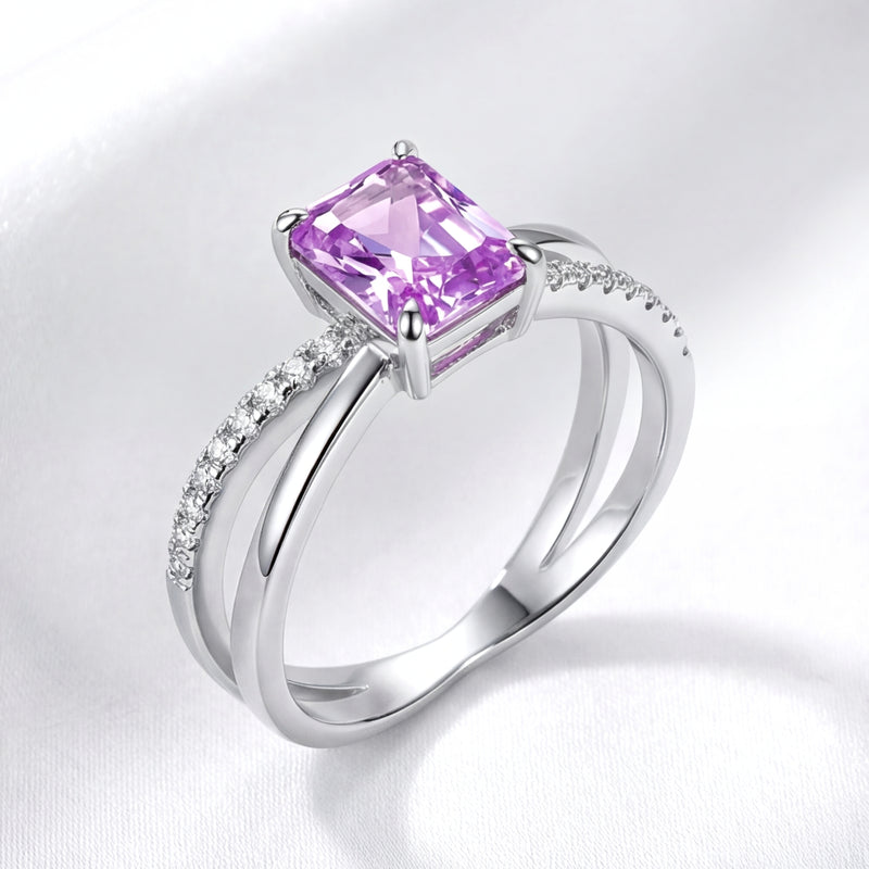 Side profile of the sterling silver Evanthe ring showing the bypass setting and emerald-cut amethyst on white fabric.