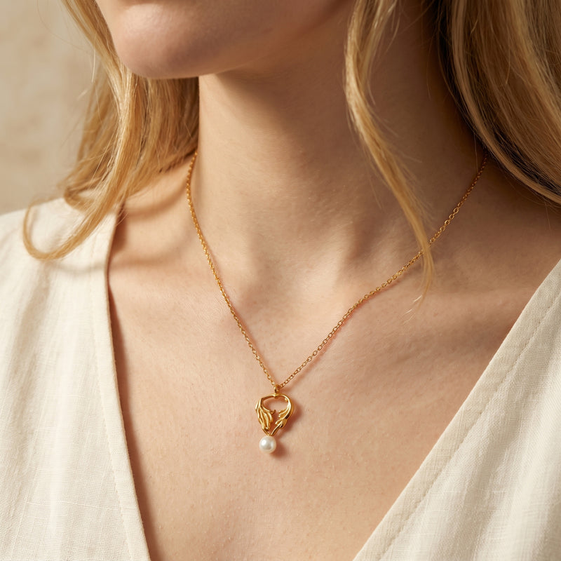 Model wearing the gold-tone leaf pendant necklace with a white pearl drop against a white top.