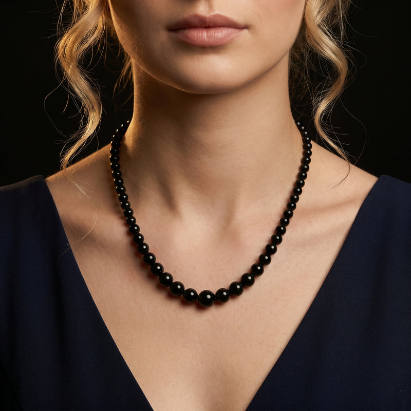 Model wearing the Penumbra graduated natural black onyx bead necklace against a dark background.