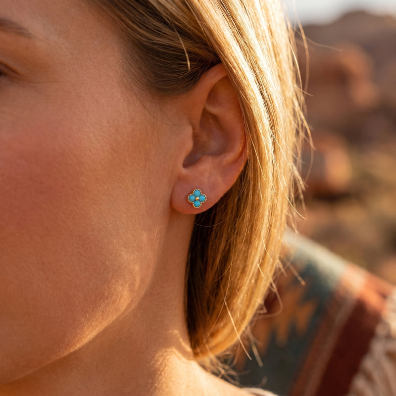 Close-up of a woman wearing a gold clover stud earring featuring four vibrant turquoise cabochons.