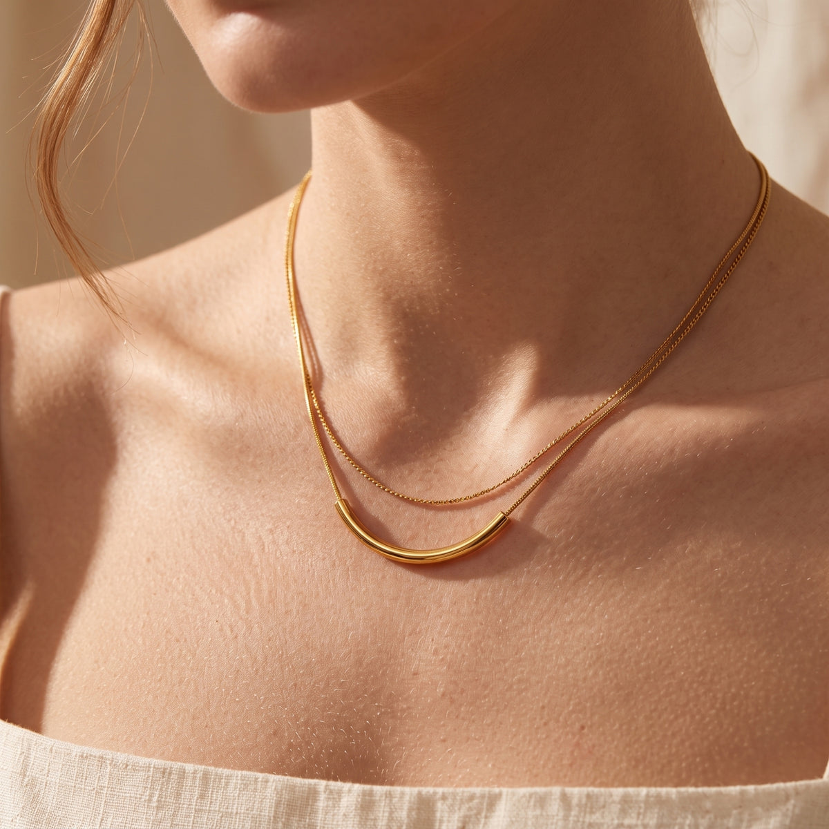Close-up of a model wearing the gold-tone double-strand necklace with a smooth curved arc bar pendant.