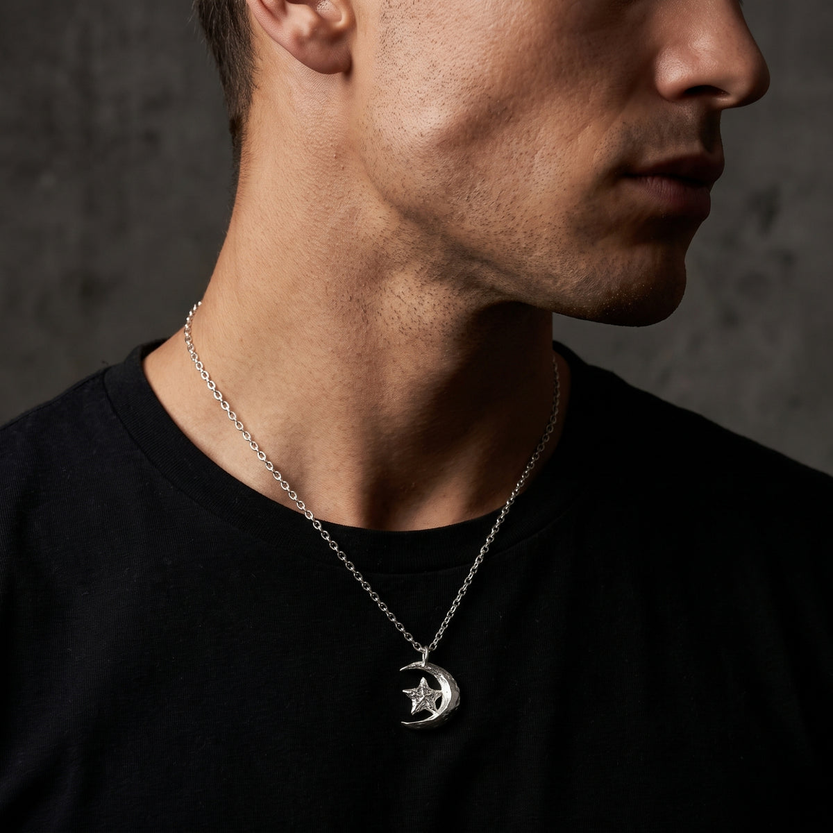 Side-profile view of a man wearing the silver crescent moon and star pendant over a black crewneck.