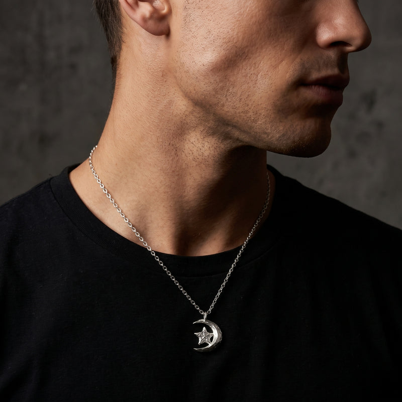 Side-profile view of a man wearing the silver crescent moon and star pendant over a black crewneck.