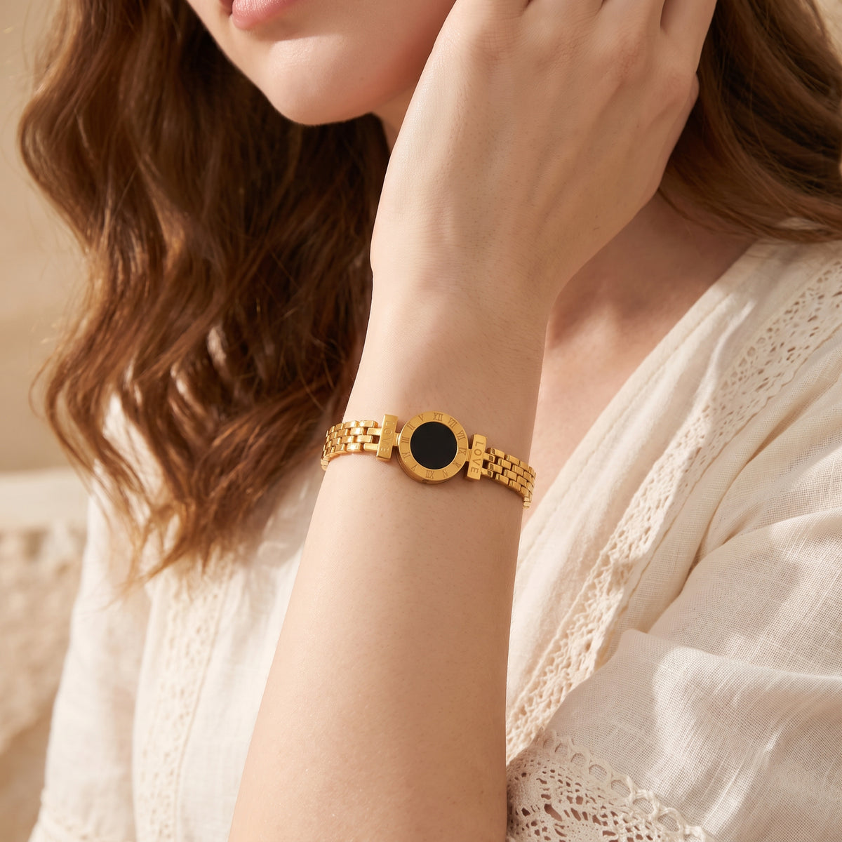 Gold-tone bracelet with a black Roman numeral medallion and linked band worn on a woman's wrist.