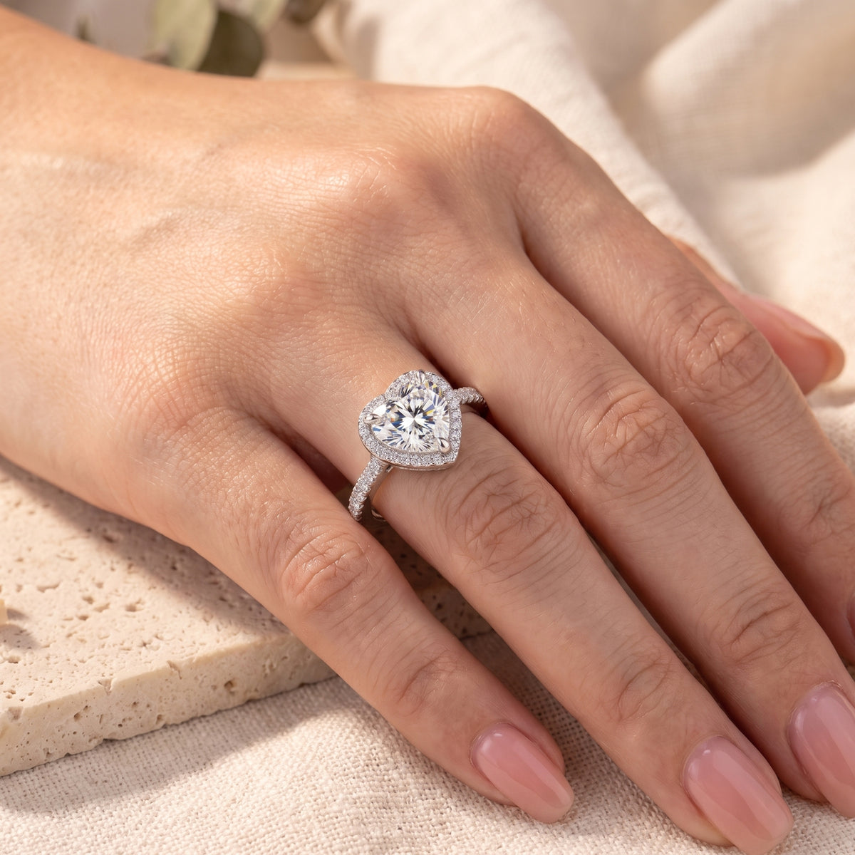 Angled view of a silver heart-shaped halo ring with a simulated diamond worn on a hand.