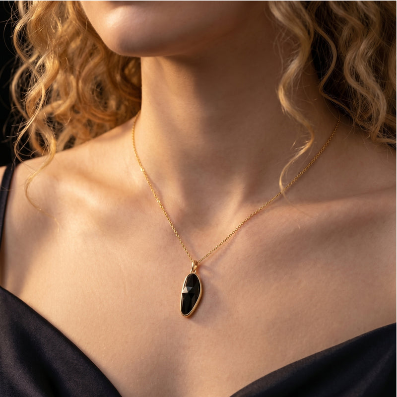 A model wearing the Morgana gold necklace with a faceted irregular-cut natural black onyx pendant.