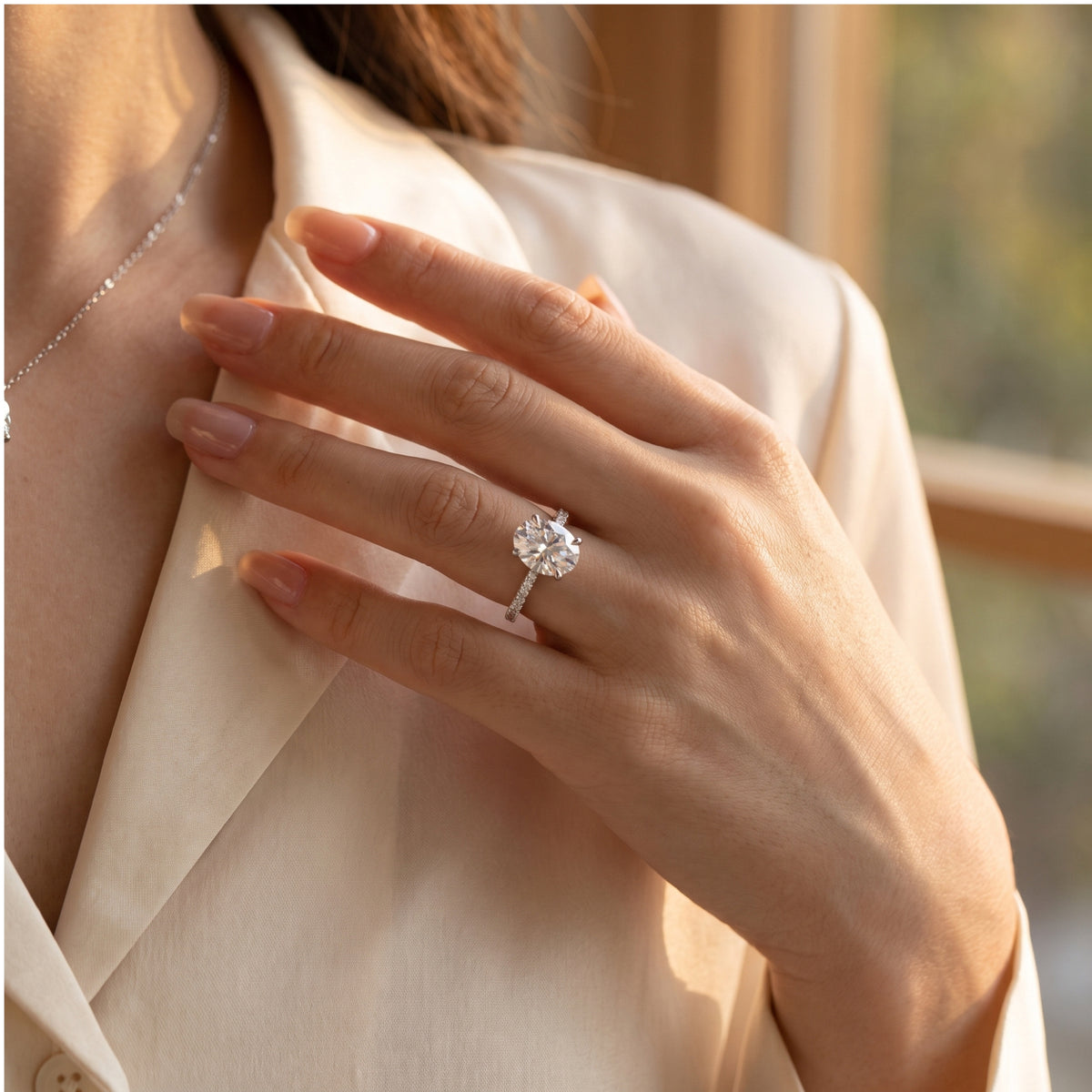 Silver ring with an oval center stone worn on a hand against a white jacket.