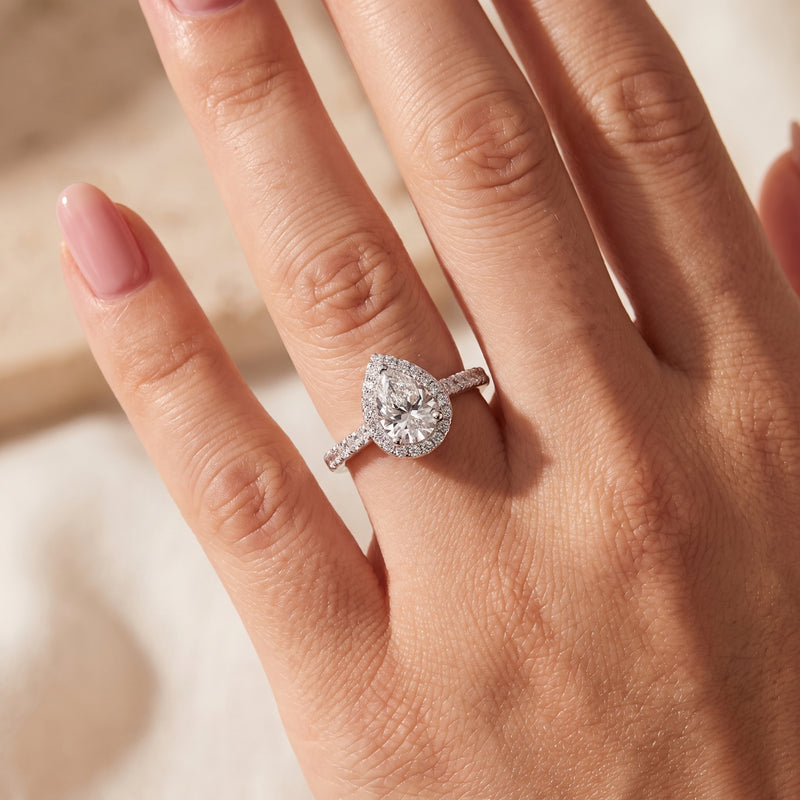 Close-up of a hand wearing a silver pear-cut halo ring on the ring finger.