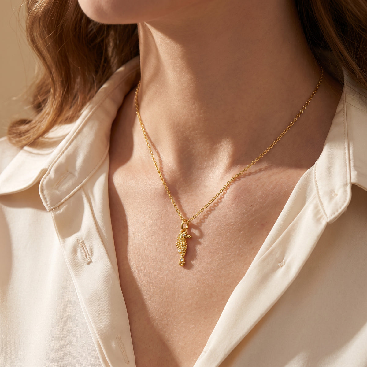 Model wearing the gold-tone seahorse pendant necklace with a light-colored button-down shirt.