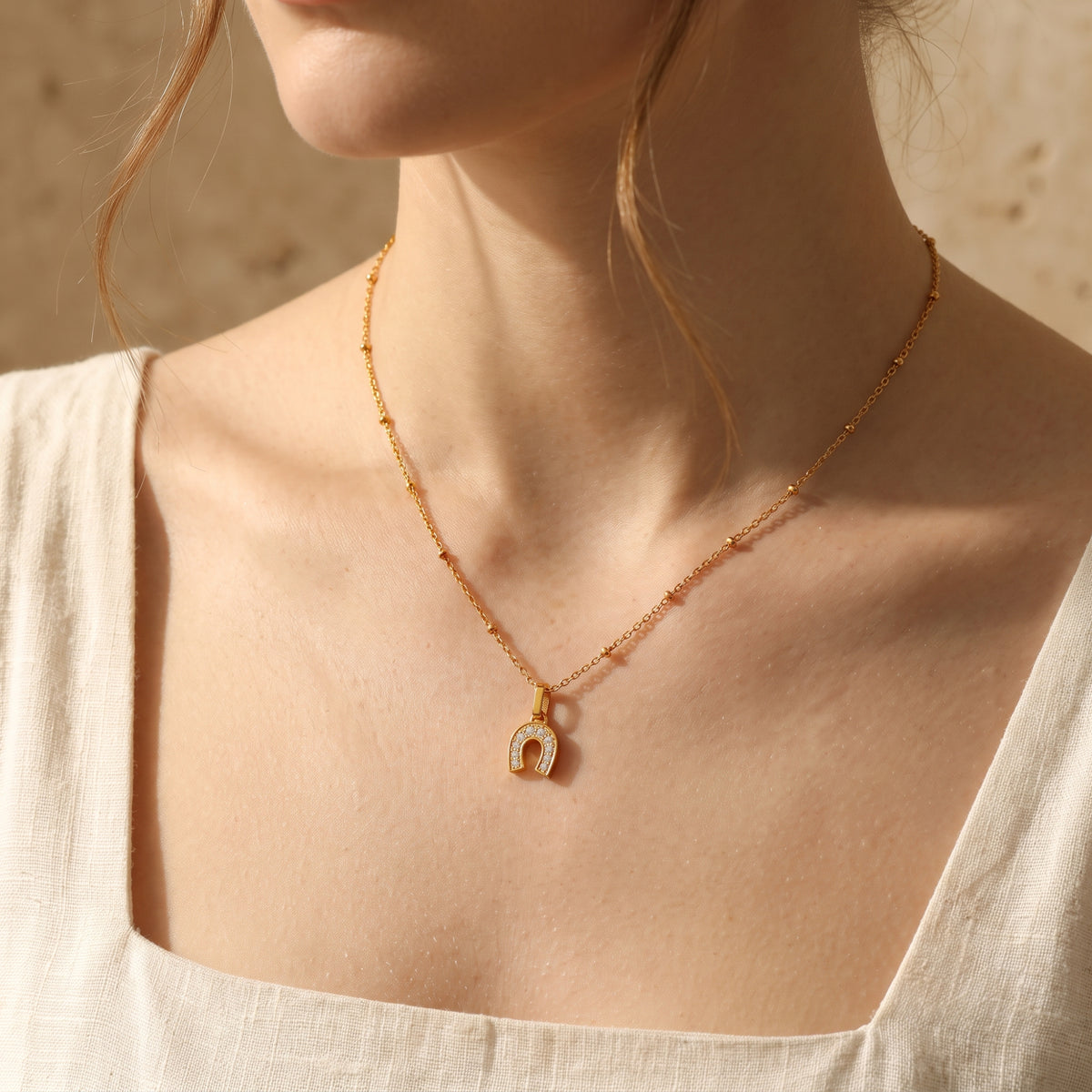 Model wearing a gold-tone horseshoe pendant necklace with clear stones on a bead-station chain.