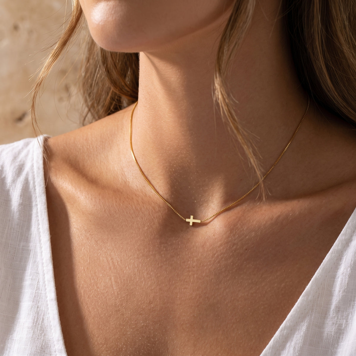Close-up of a model wearing the gold-tone sideways cross necklace on her upper chest.