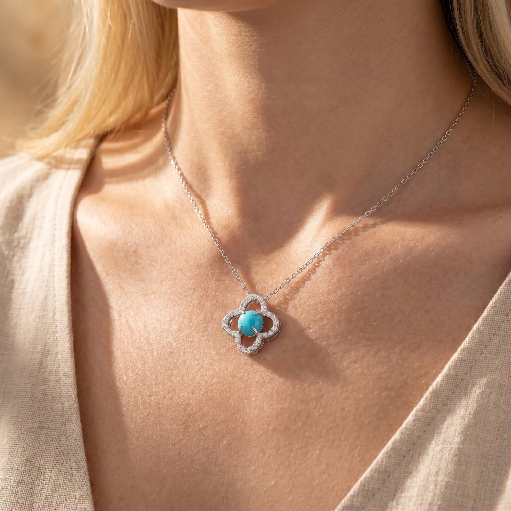Silver quatrefoil necklace with a round turquoise stone worn at the collarbone.