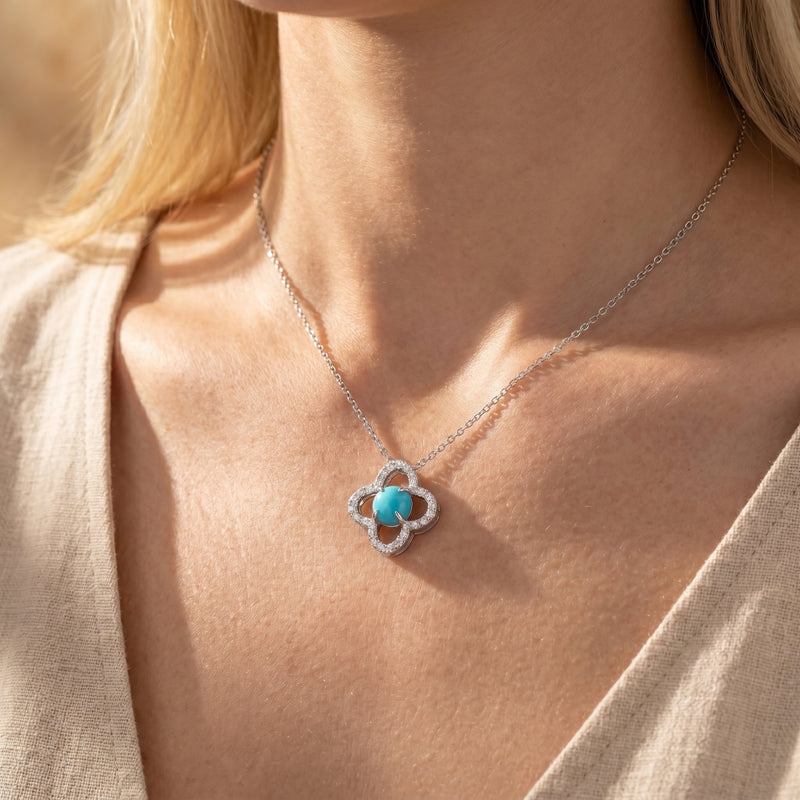 Silver quatrefoil necklace with a round turquoise stone worn at the collarbone.