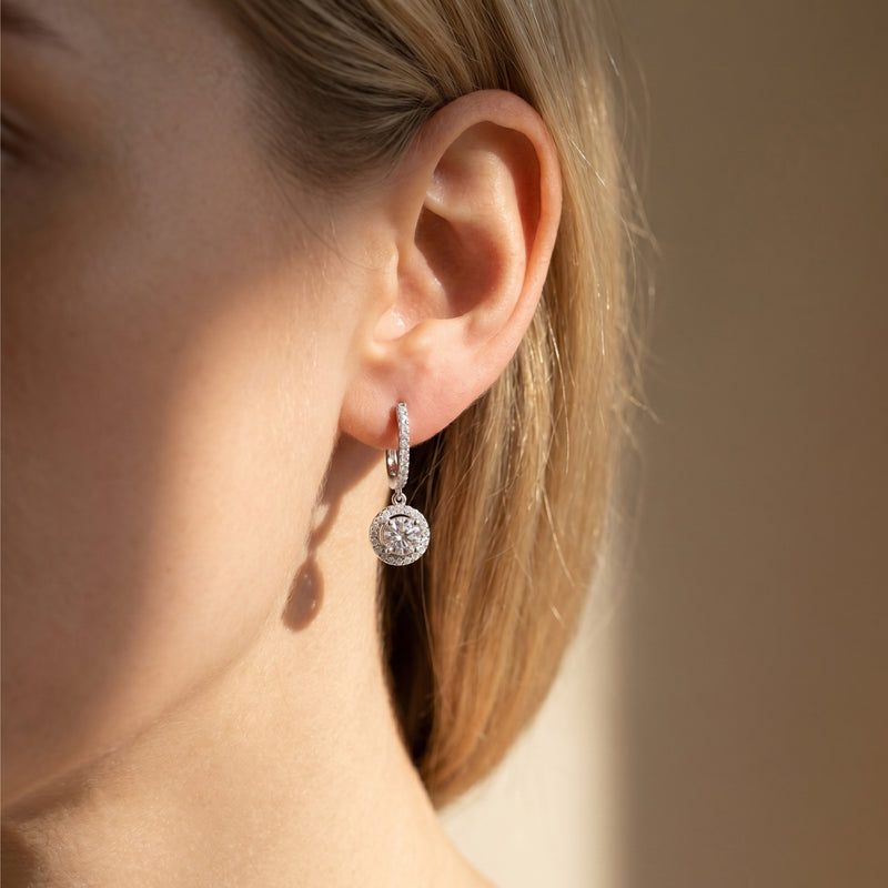 Silver round moissanite drop earring worn on a model's ear in natural light.