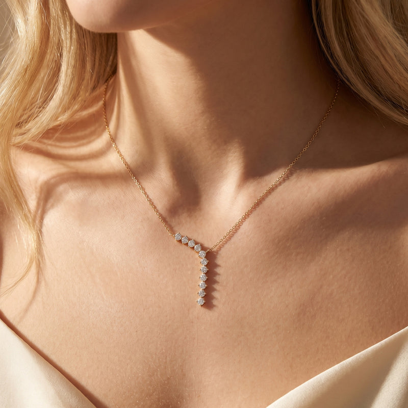 Gold curved drop necklace featuring round-cut moissanite stones worn on a model's neck.