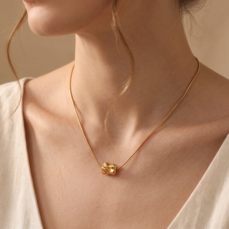 Model wearing the 18K gold finish Petra necklace featuring a sculptural molten bead on a fluid snake chain.
