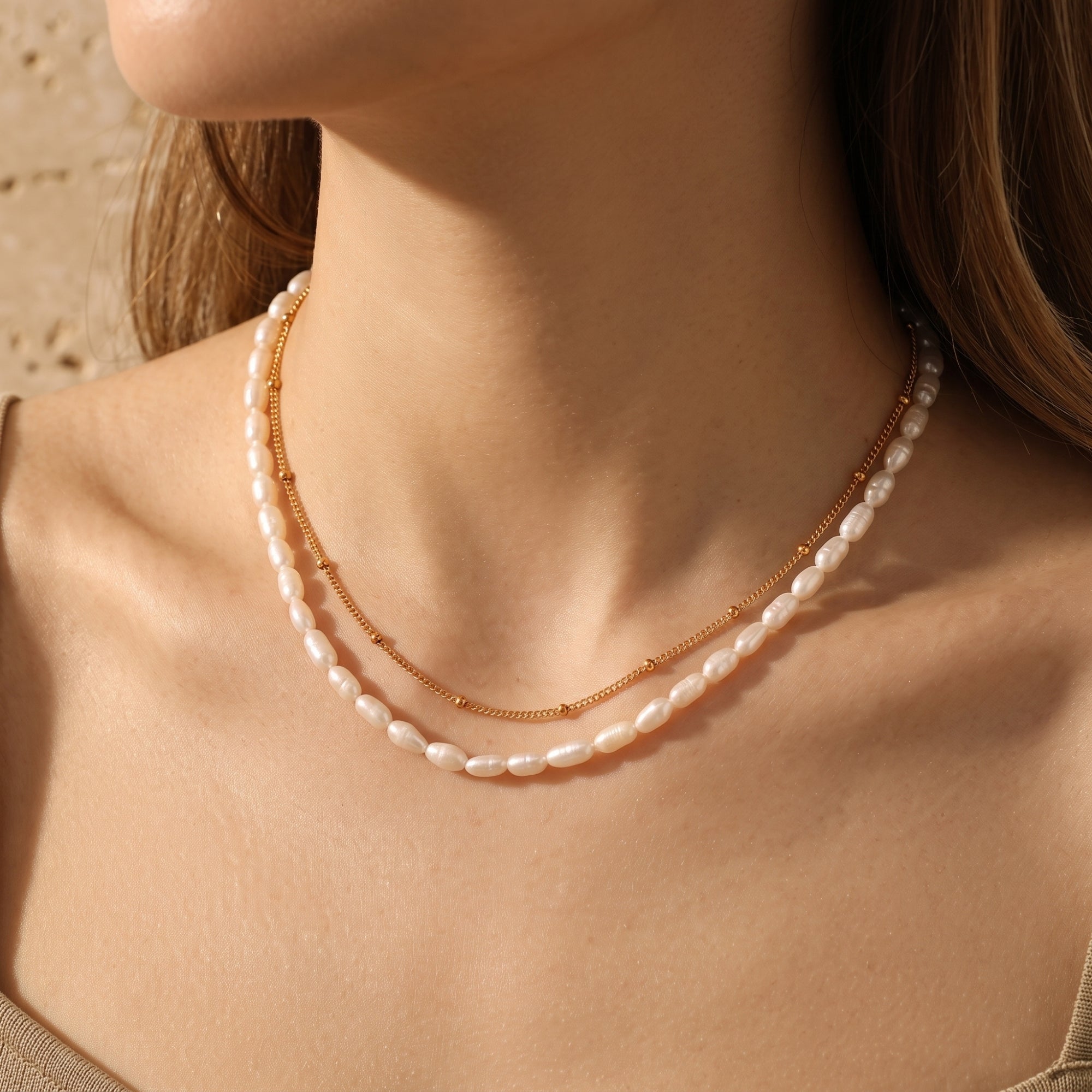 Chiara layered gold necklace with satellite chain and white freshwater pearls worn by a model.