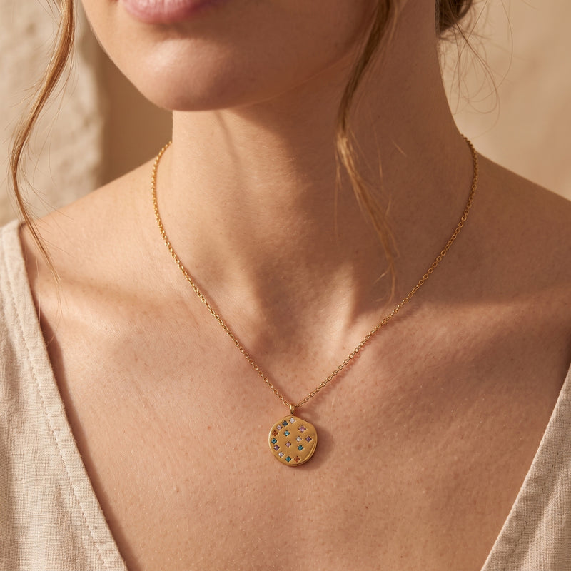 Model wearing the 18K gold Astraline pendant necklace featuring a circular medallion with rainbow CZ crystals.