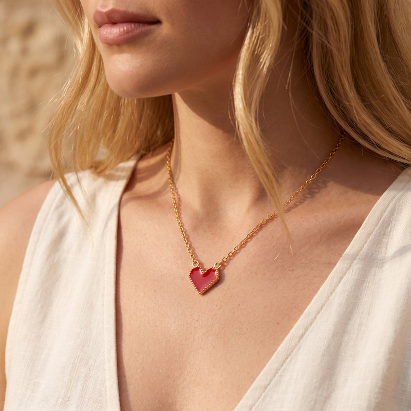 Model wearing the red heart pendant necklace on a gold-tone chain with a white V-neck top.