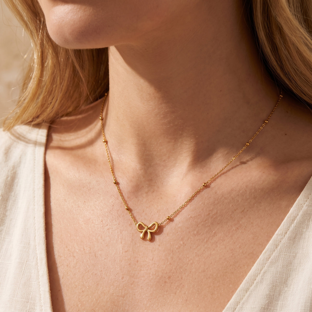Close-up of a model wearing the gold-tone bow station necklace on her upper chest, with a cream top visible.