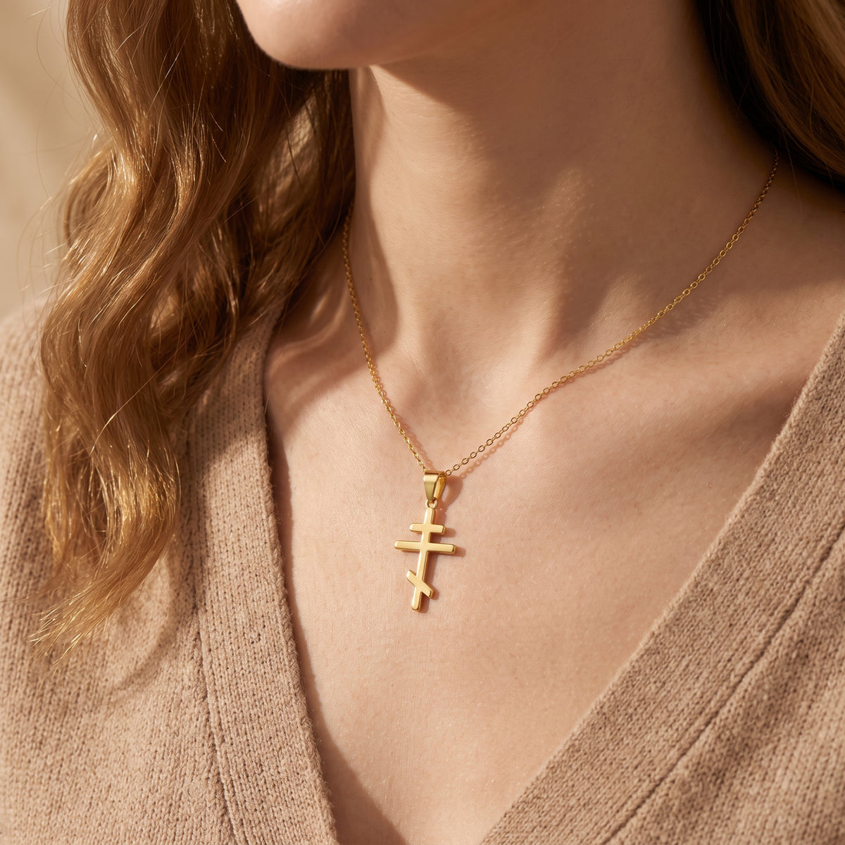 Gold-tone Eastern cross pendant necklace worn around the neck over a beige knit top.
