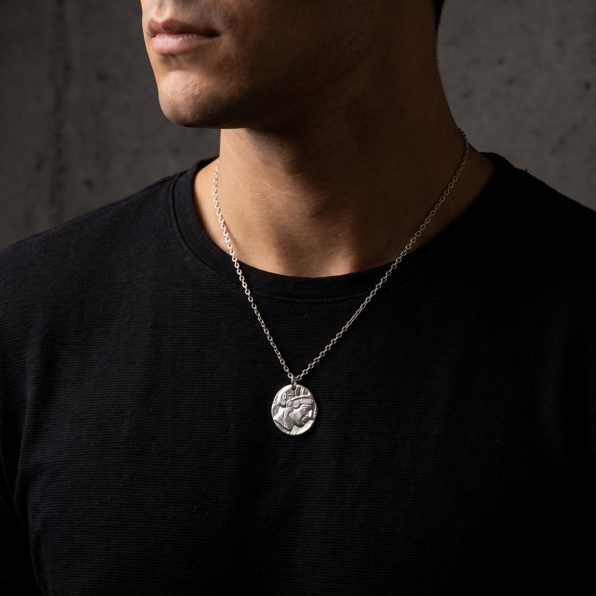 Silver Athenian coin pendant necklace shown worn over a man's black crewneck shirt.