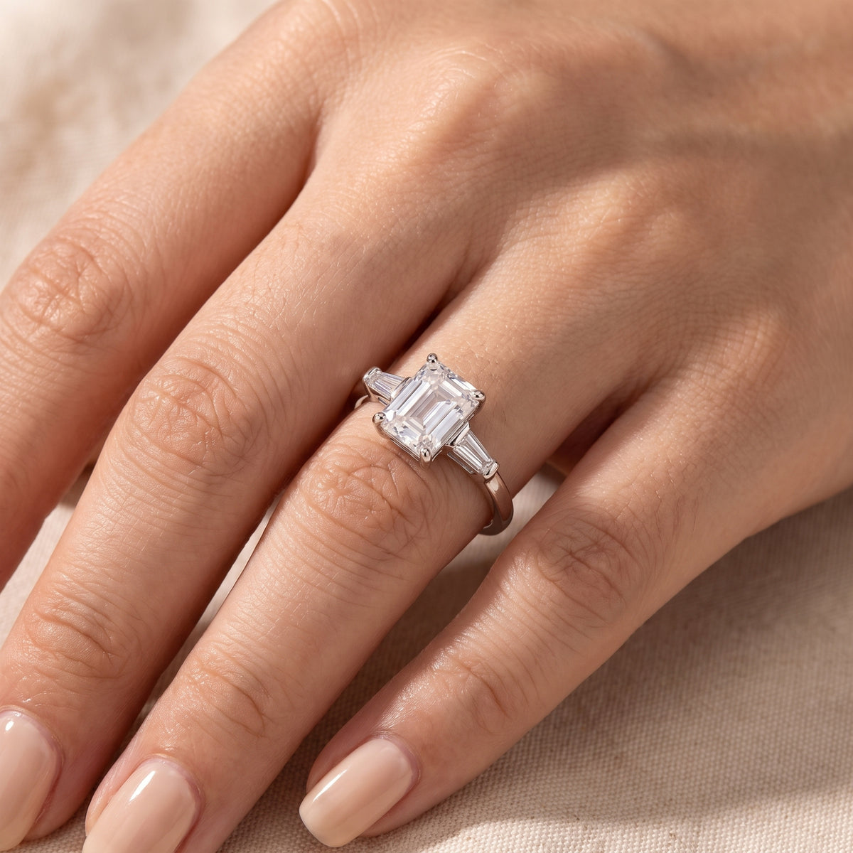 Close-up of a hand wearing a silver three-stone ring with an emerald-cut center stone and tapered baguette side stones.