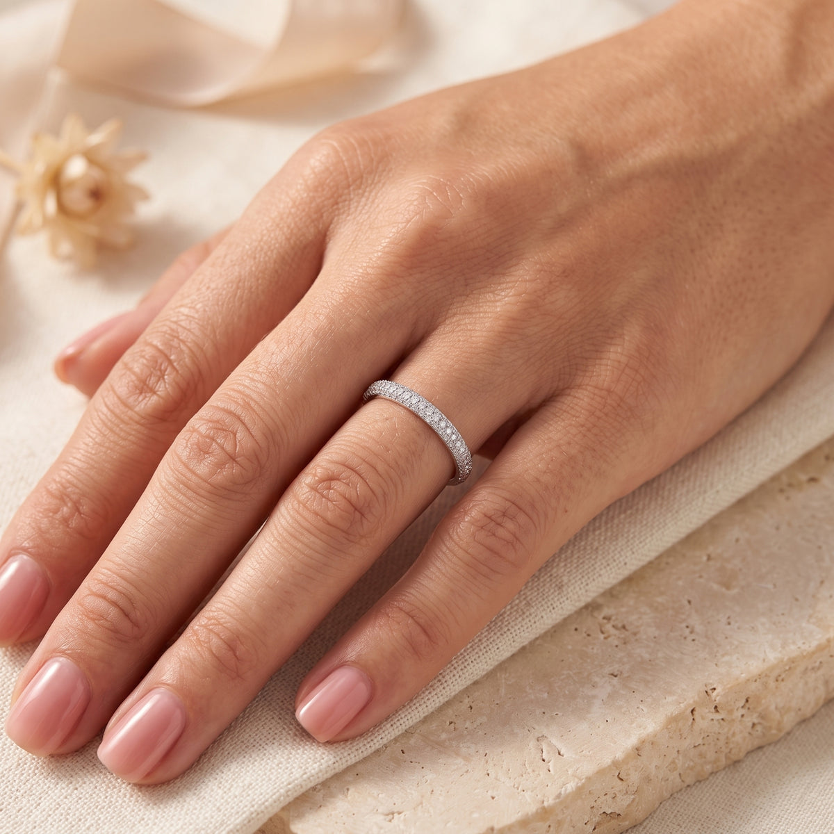 Silver multi-row pavé band ring worn on a hand over cream fabric and a beige stone block.