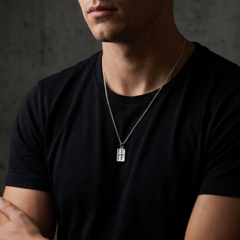 Front view of a man in a black t-shirt wearing the silver textured rectangular cross necklace.