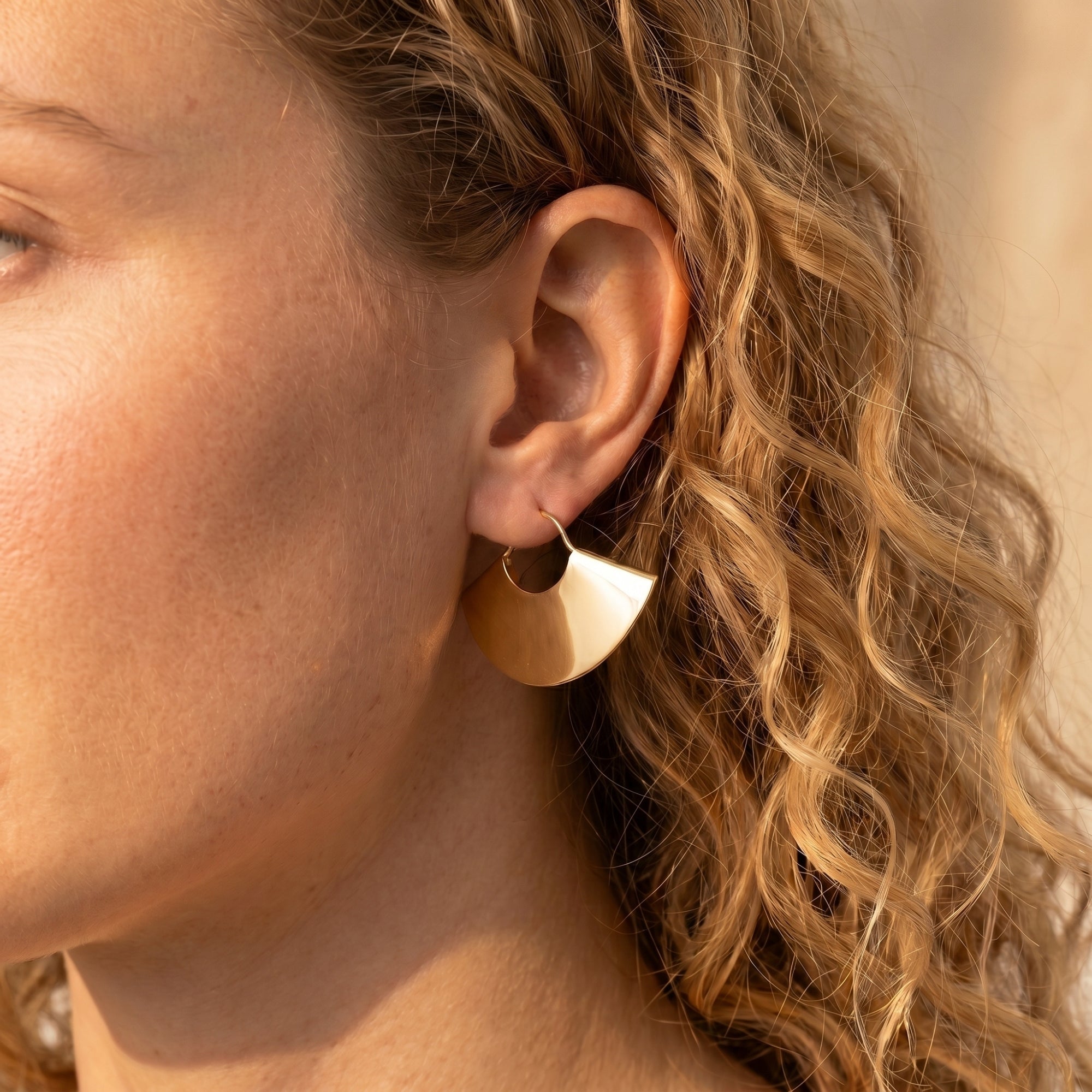 Model wearing a gold fan earring in 18K gold PVD stainless steel.