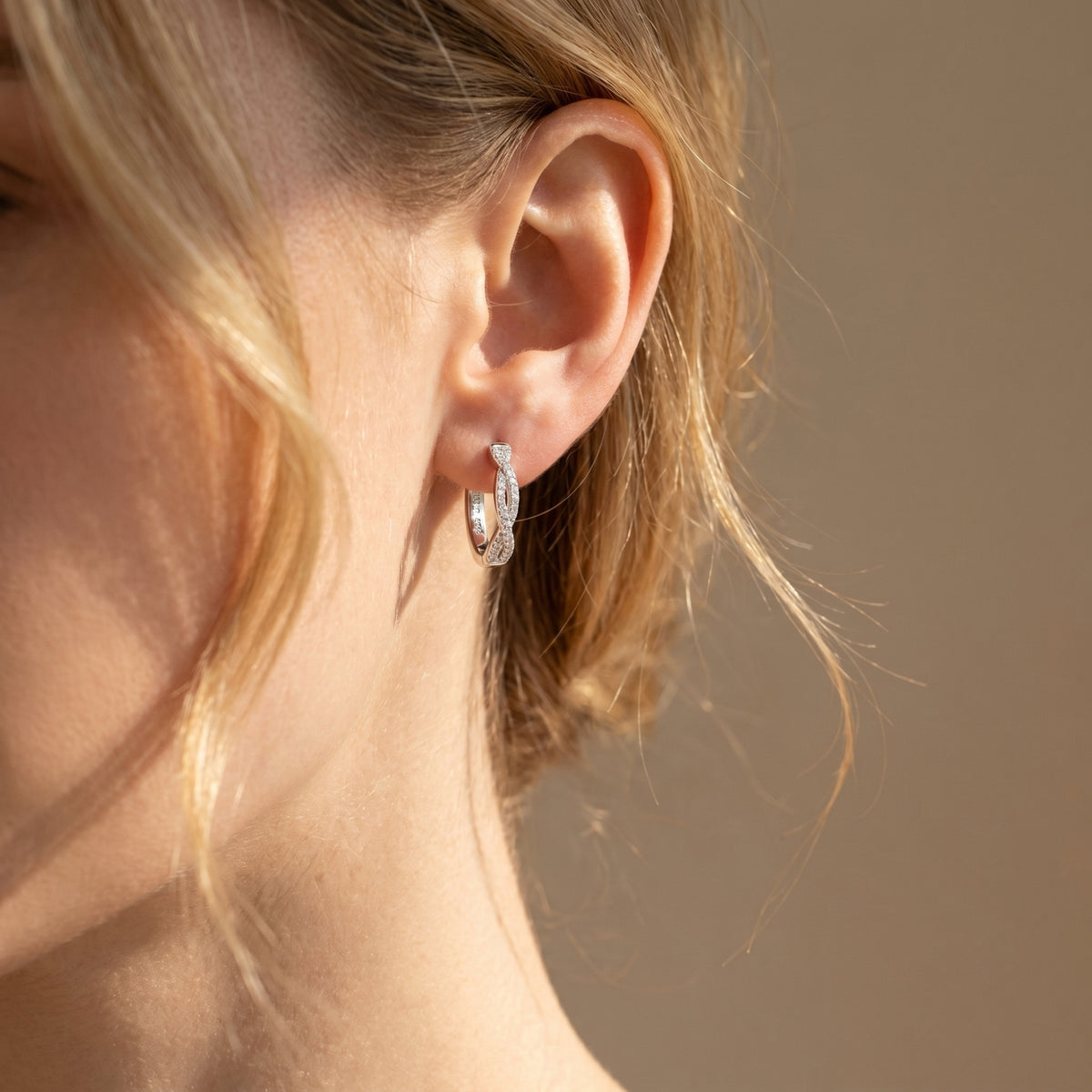 Silver moissanite twisted hoop earring worn on a woman's ear.