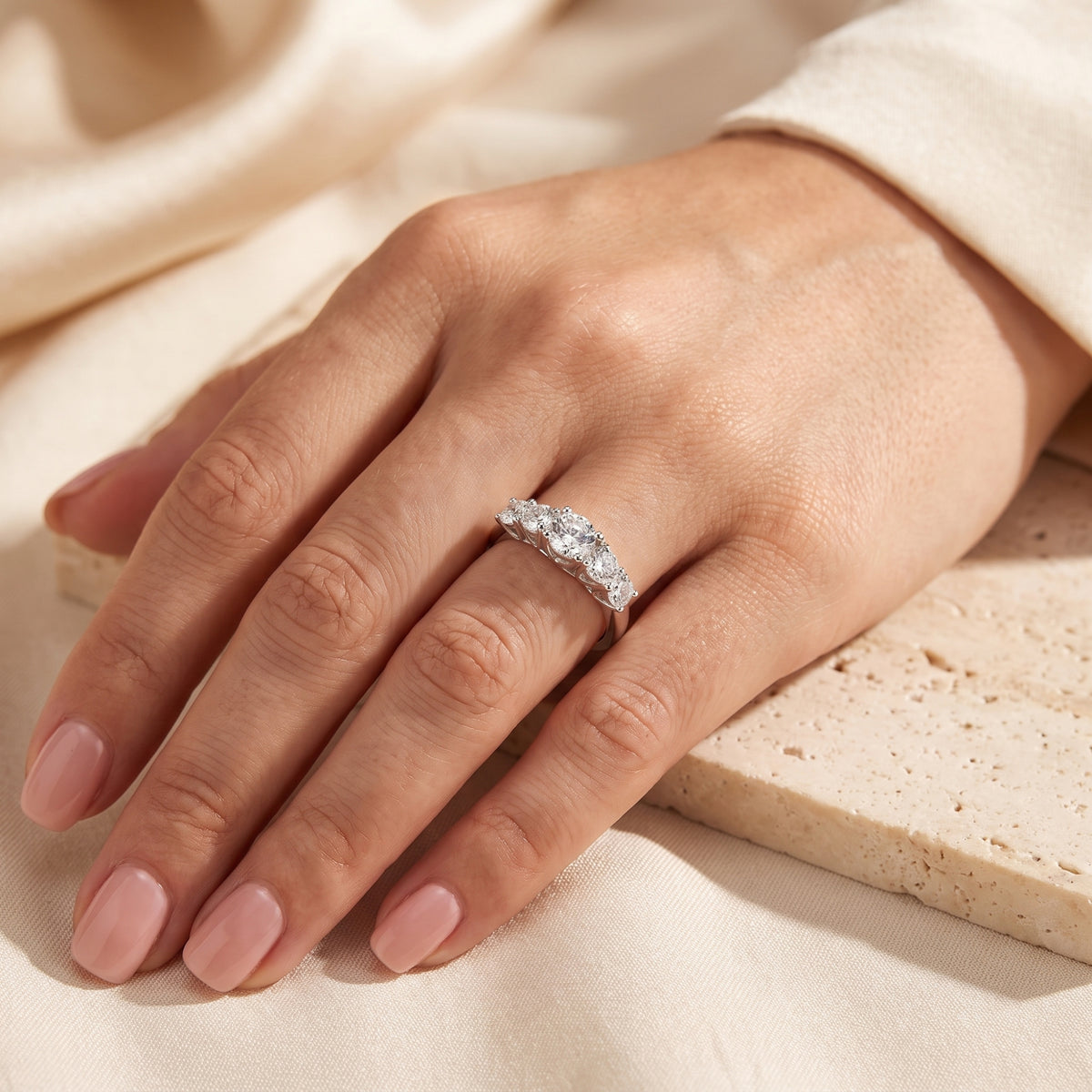 Hand wearing the five-stone silver ring with graduated round clear stones on a ring finger.