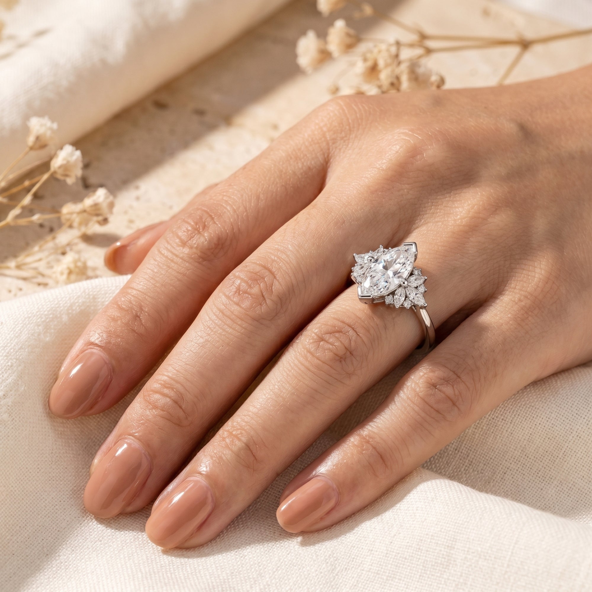 Silver 2-carat marquise moissanite ring worn on a woman's hand against a neutral fabric background.