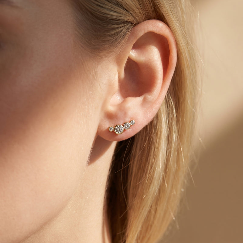 Gold moissanite climber earring with round stones worn on a woman's earlobe.