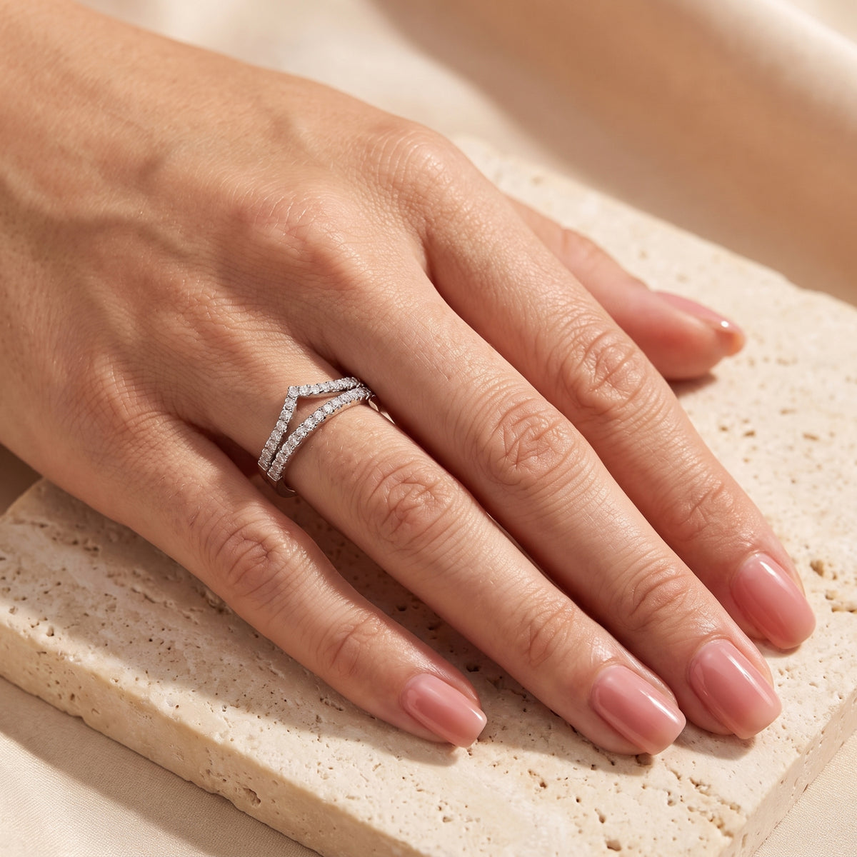 Close-up of a hand wearing the silver double chevron ring set on the ring finger over a beige stone surface.