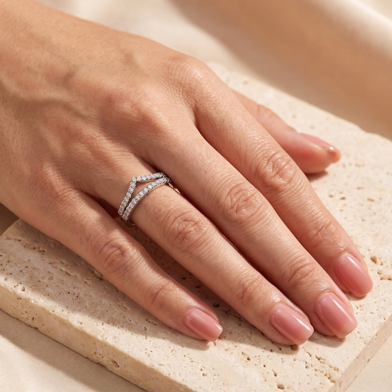 Close-up of a hand wearing the silver double chevron ring set on the ring finger over a beige stone surface.