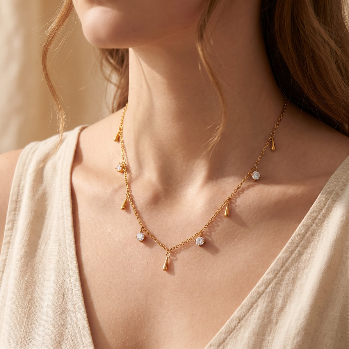 Gold-tone station necklace with clear stones and smooth droplet charms worn on a woman's neck.