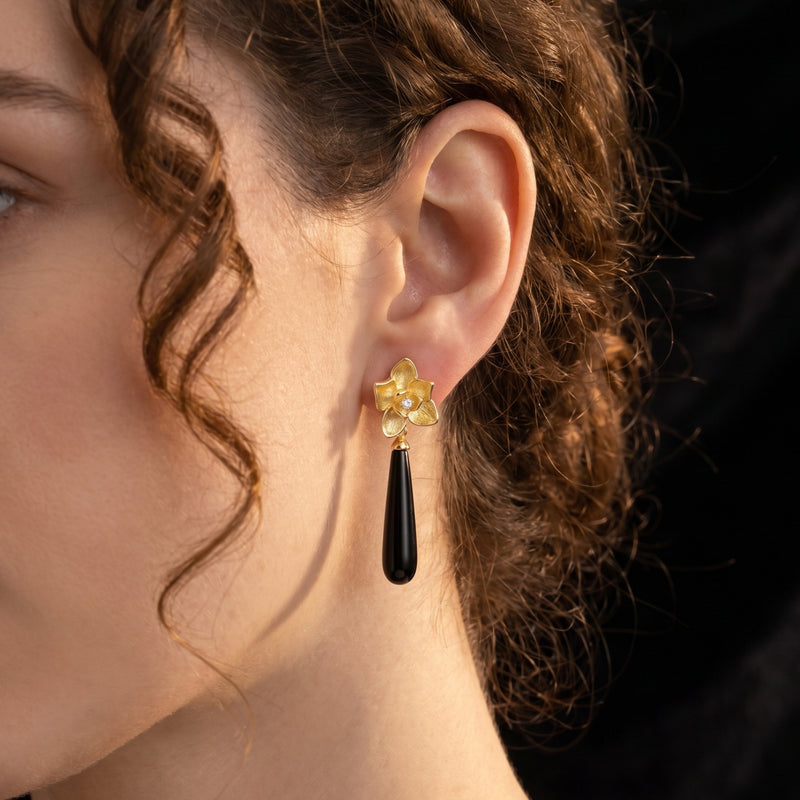 Calla floral drop earring with an elongated black onyx stone worn on a model's ear, crafted in solid gold.
