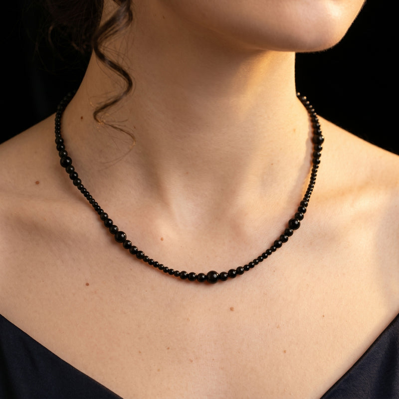 Woman wearing the graduated natural black onyx bead necklace against a dark background.
