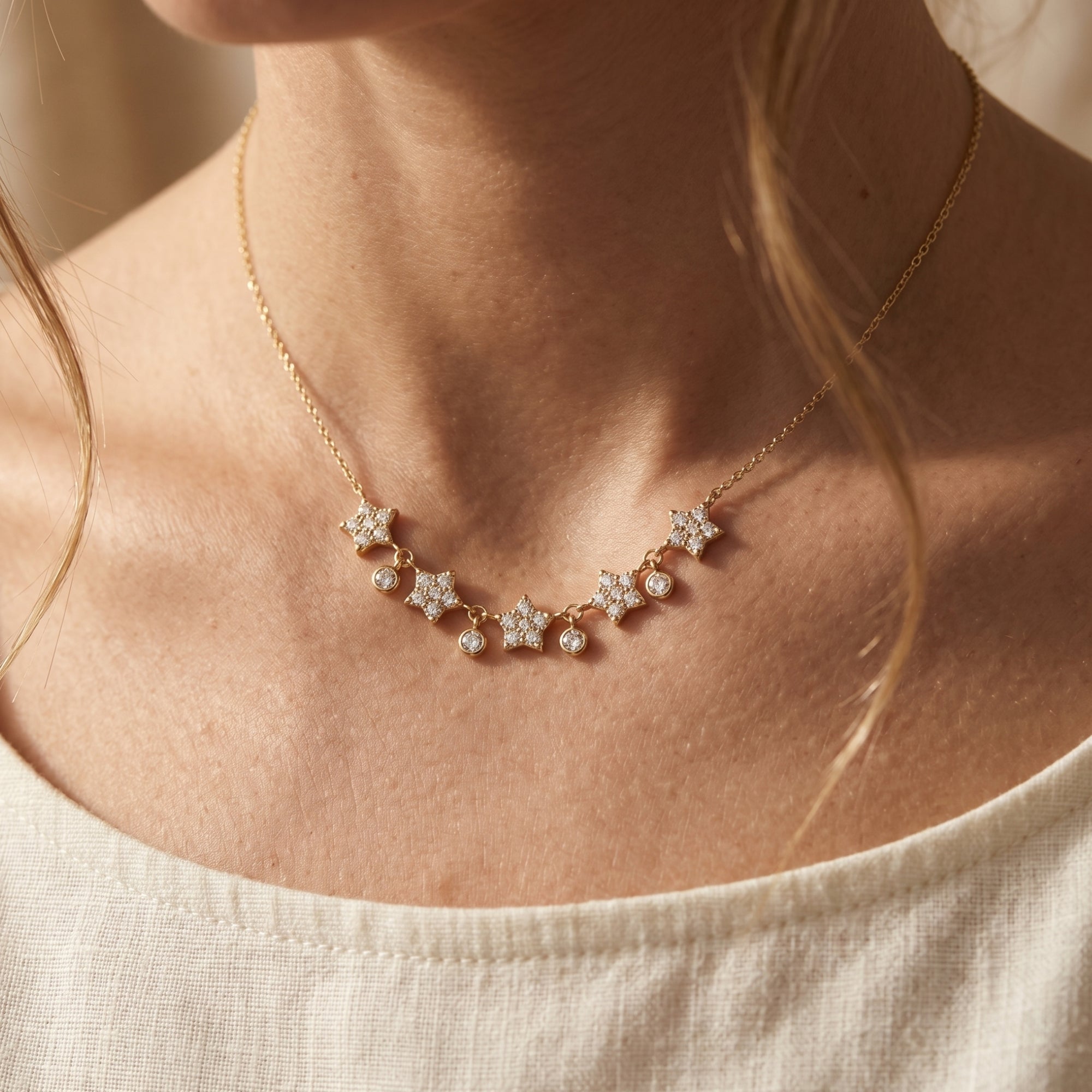 Woman wearing the gold Astrielle moissanite star pendant necklace with five cascading star motifs.